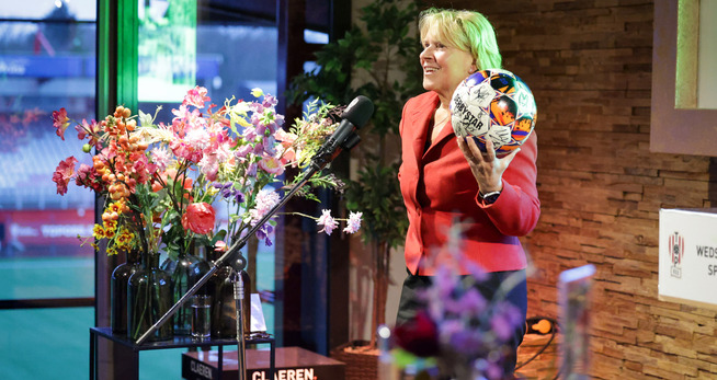 Een vrouw die een bal vasthoudt en voor een microfoon staat